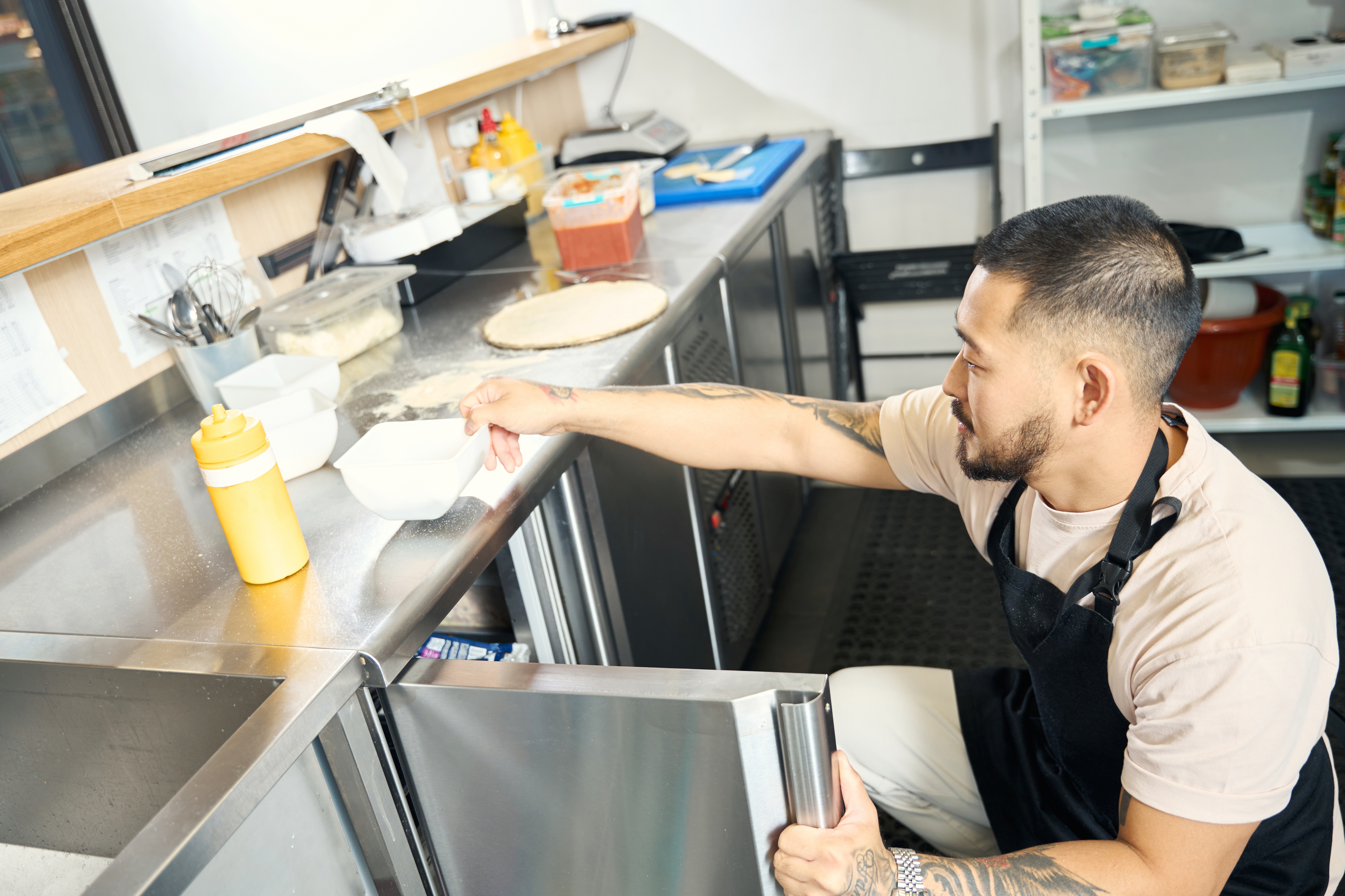 A chef reaches into a lowboy to pull out some ingredients to work on.